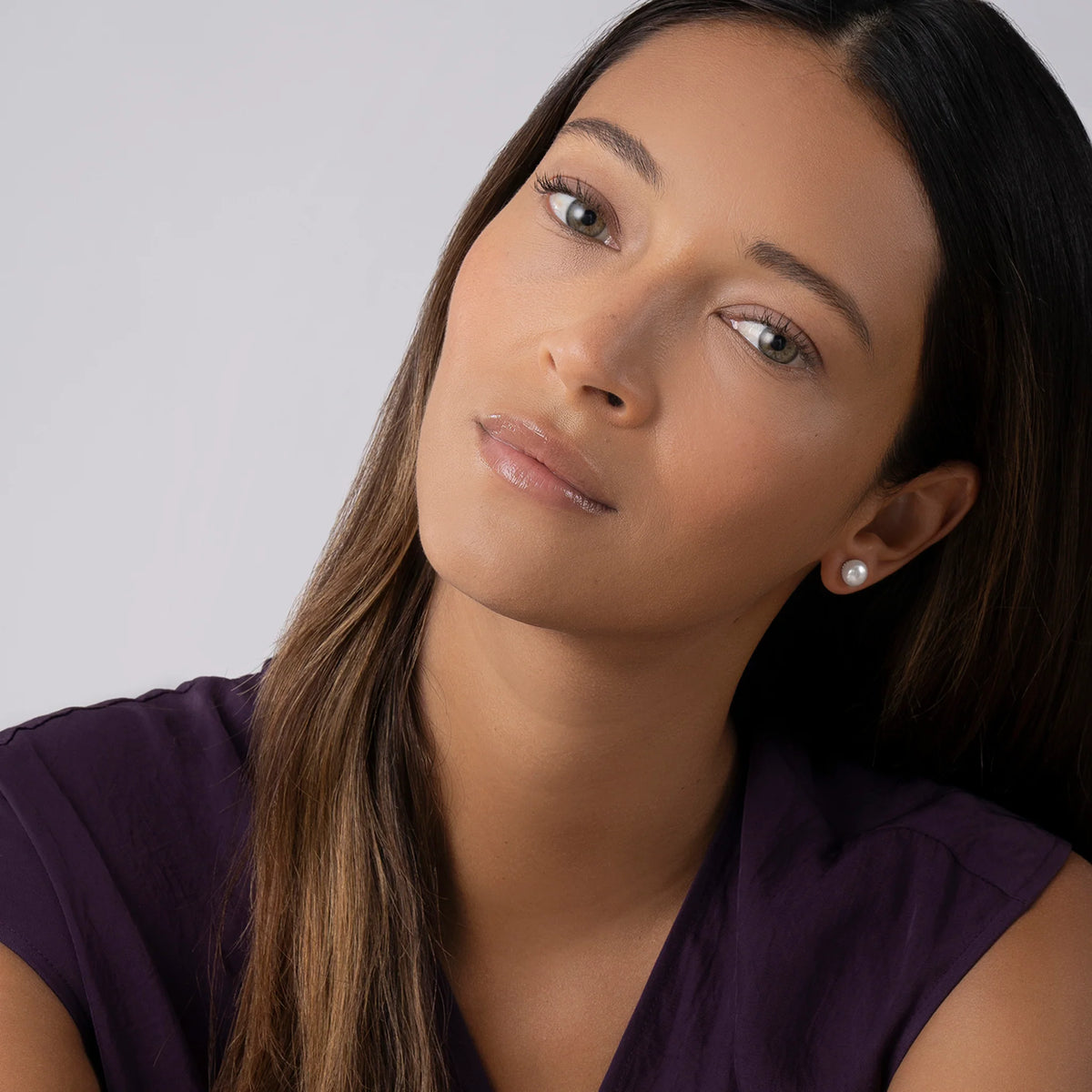 woman wearing purple shirt and pearl earrings on a grey background