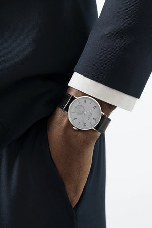 A man wearing a dark suite and watch on wrist on a white background
