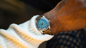 Close-up of a wrist wearing a watch with a blue face and brown leather strap.
