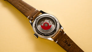 Watch with a brown leather strap and visible mechanical components on a beige background