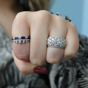 Hand wearing a blue sapphire band (0.21 ctw) with diamond accents beside a pavé diamond dome band