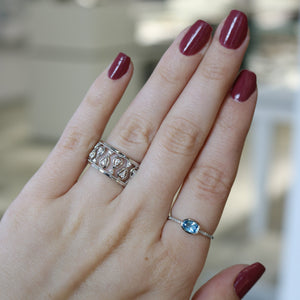 Left hand with burgundy nails, ornate silver band on middle finger and delicate silver ring with blue gemstone on ring finger