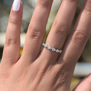 Hand with pale-pink manicure wearing a thin band of five pear-shaped diamonds on the ring finger.