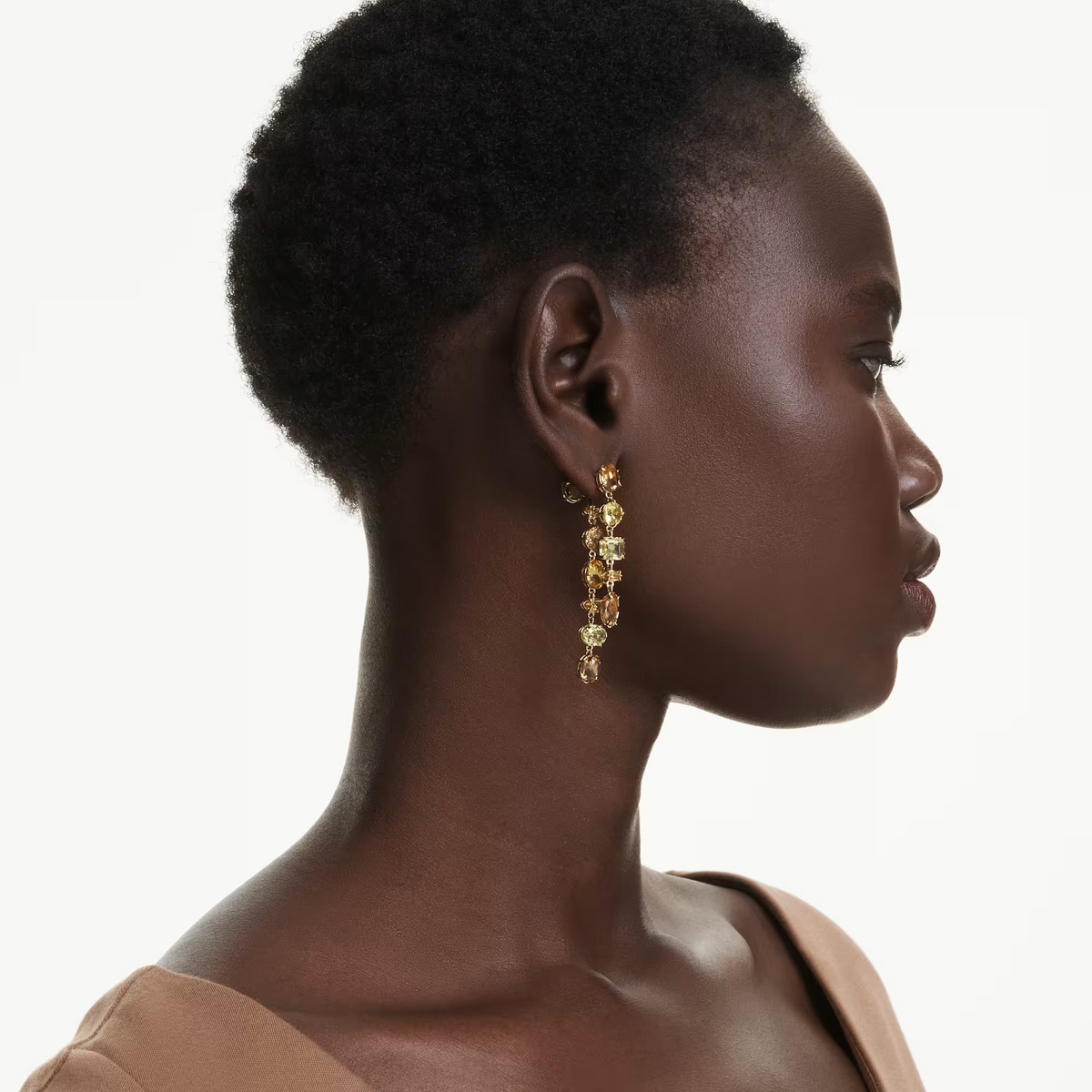Side profile of model wearing Gema Drop Earrings gold-tone asymmetrical drops with prong-set stones on white background