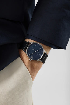 Person wearing a dark blue watch with a navy suit and white slacks.