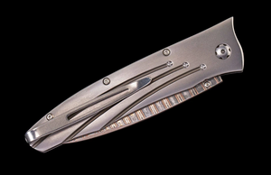 Closed William Henry Saturn III folding knife with titanium handle and decorative milled spine on black background.