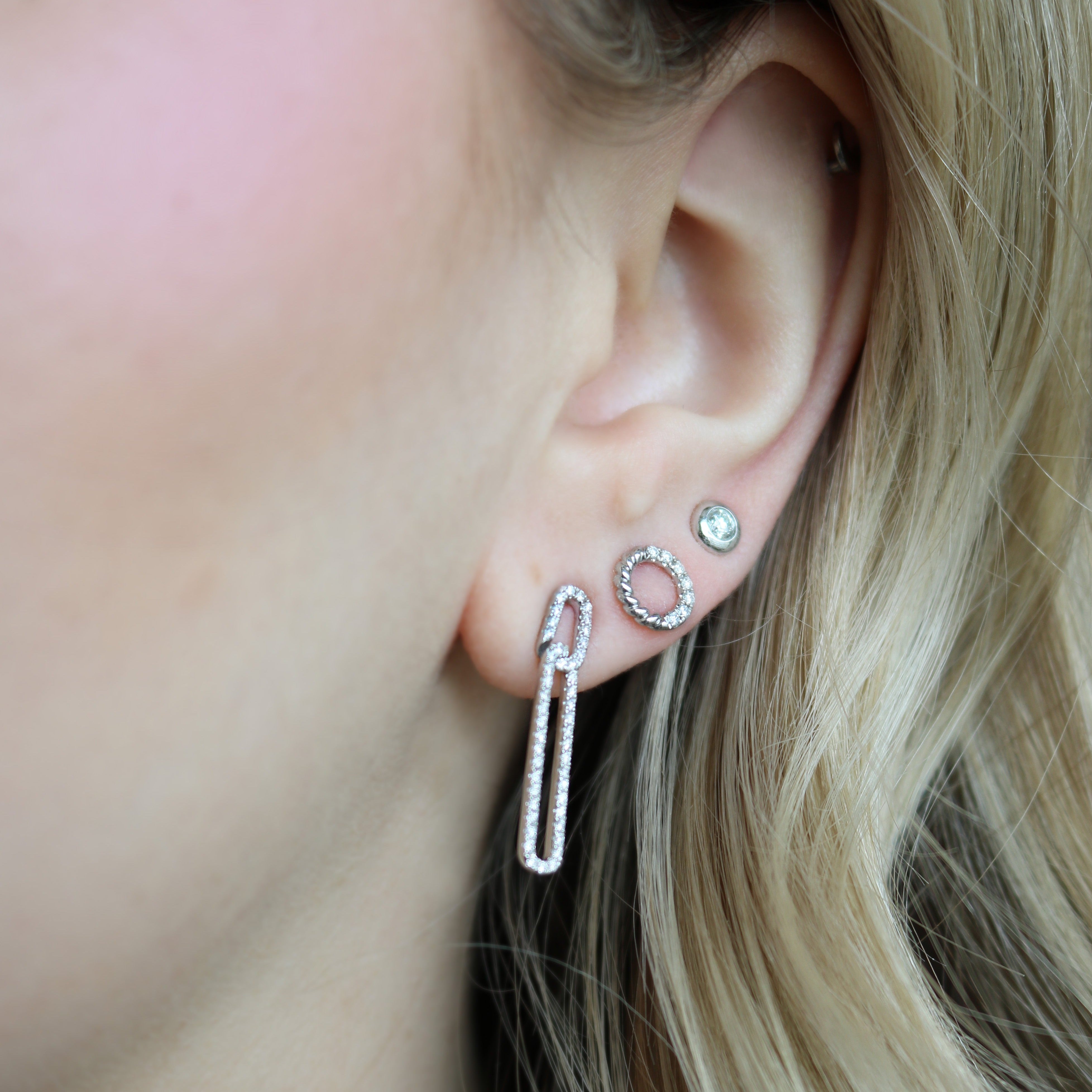 Close-up of left ear wearing Diamond Circle Stud Earring in 14K white gold, diamond halo beside two small studs, blonde hair