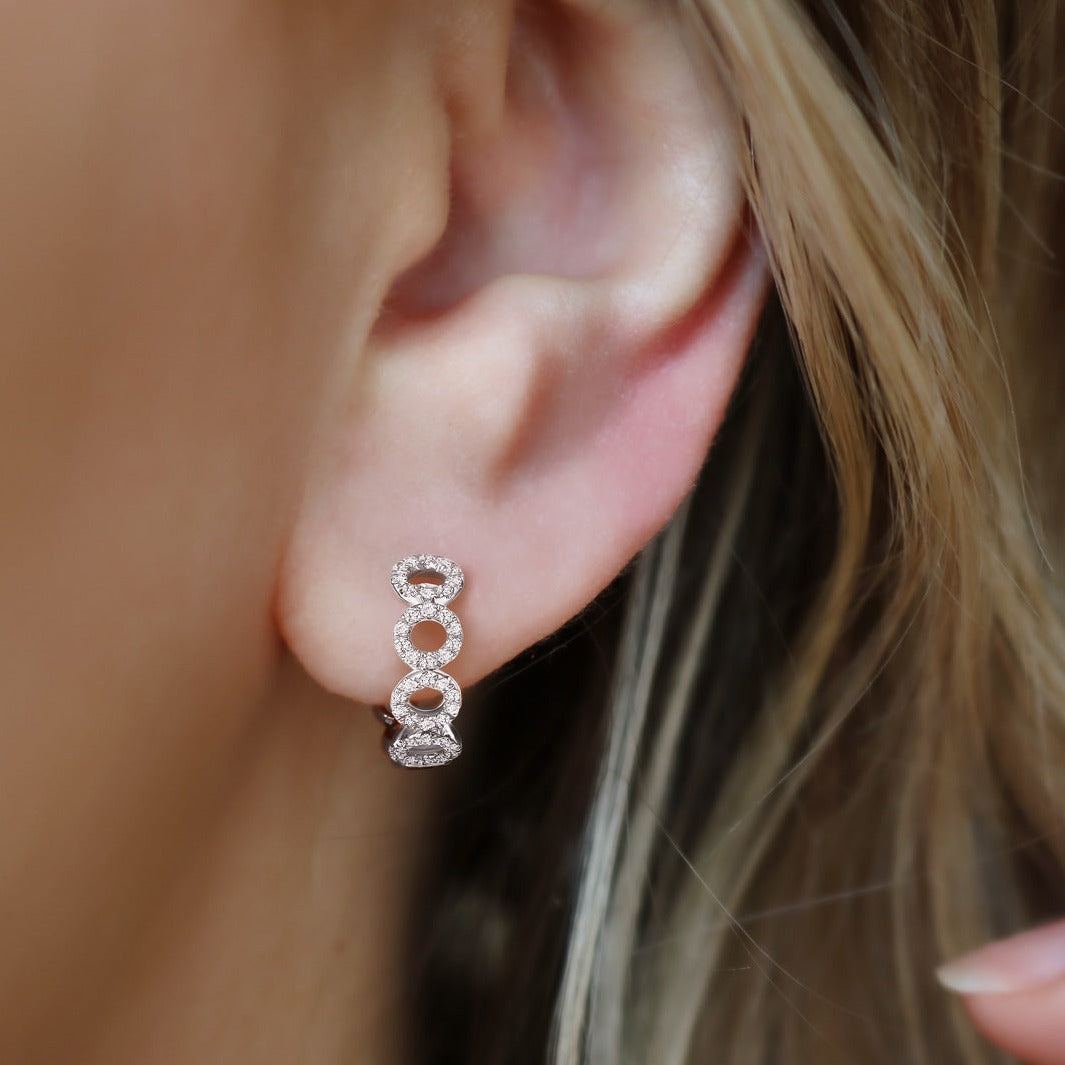 Close-up of 14k white gold Uneek earrings on model's ear, three linked oval pavé diamonds against blurred hair