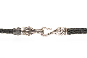 Close-up of braided black leather necklace showing engraved sterling silver hook clasp on white background