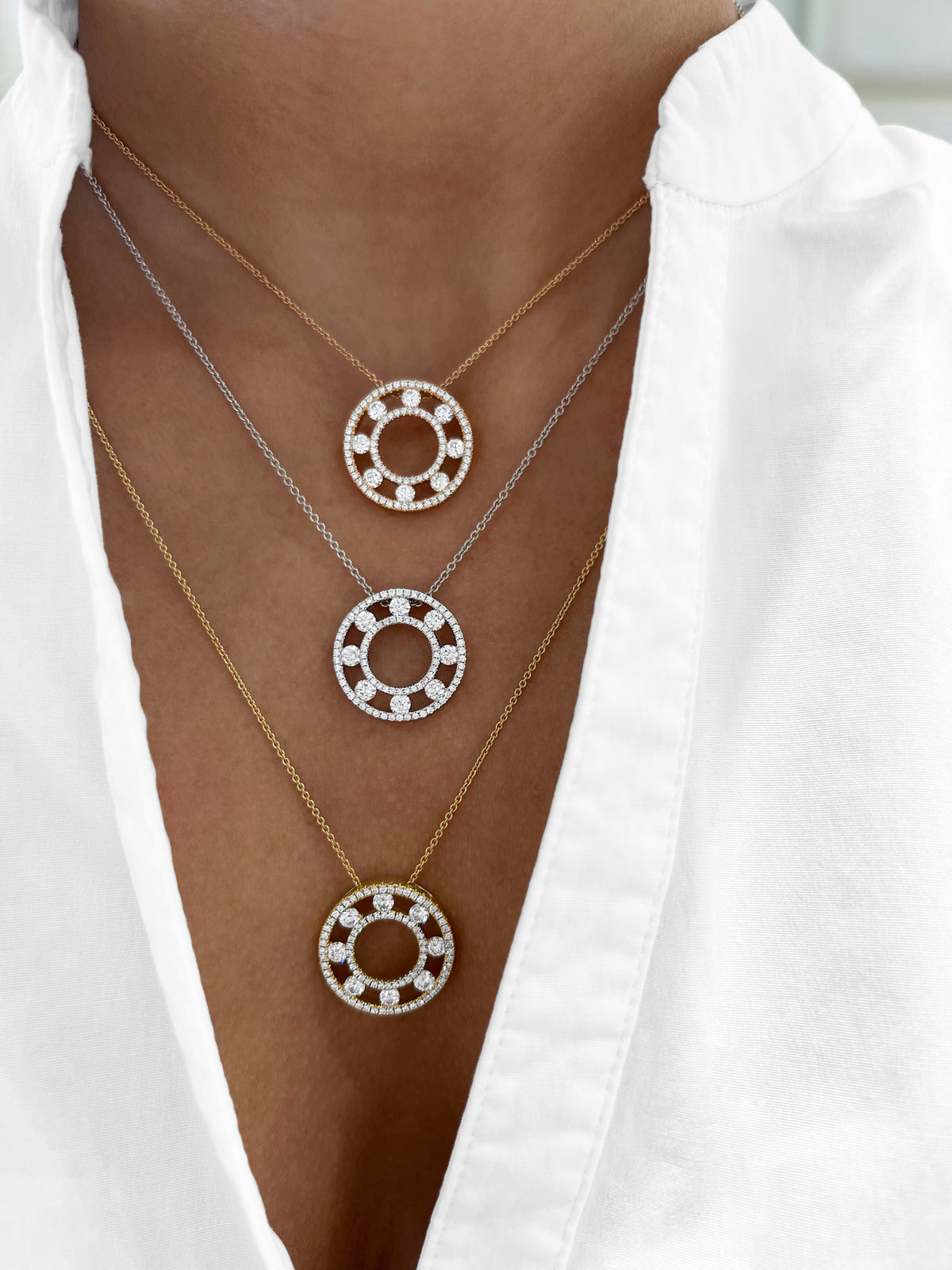 Close up of three Floating Diamond Pavé Circle pendants showing pavé diamonds on mixed gold chains on a white shirt