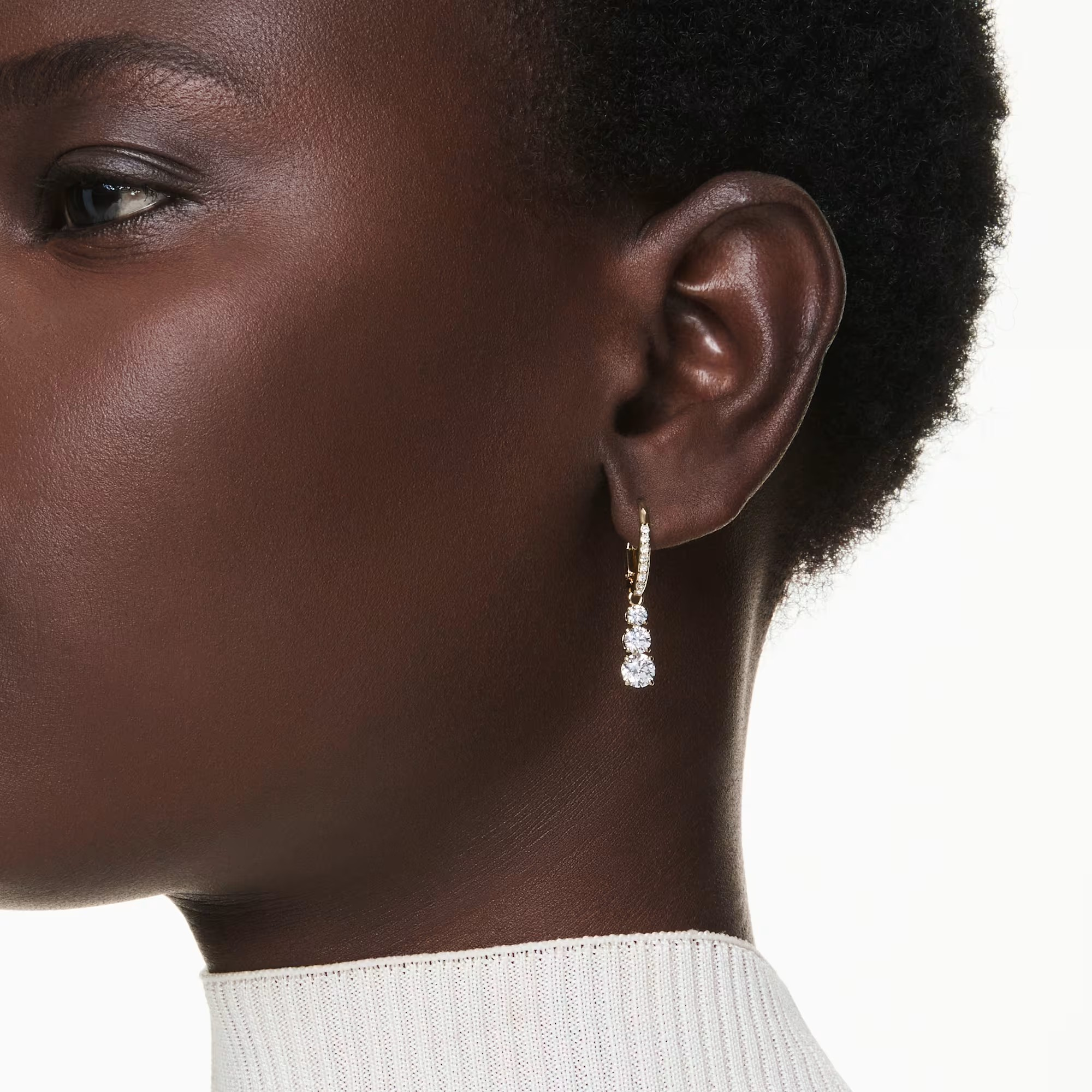 Close-up side view of Stilla Attract hoop earrings on model, gold hoops with three clear zirconia drops, white background