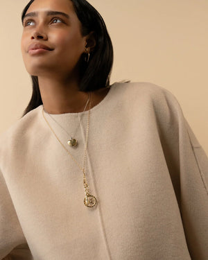 a woman wearing a beige sweater and gold necklaces on a beige background