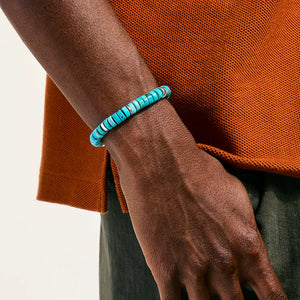 Turquoise beaded bracelet on a wrist with an orange garment in the background