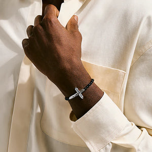 Hand wearing a bracelet with a cross charm on a white background