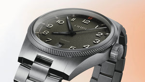 Oris watch with a dark green and silver bracelet on a gradient background