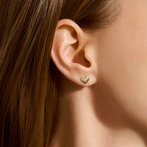Close-up of an ear wearing a gold heart-shaped earring with hair partially obscuring the view.