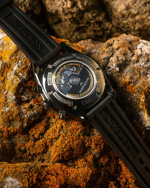 Angled close-up of Adventure Sport Chrono caseback displaying movement and Limited Edition rotor on orange lichen rock