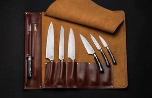 Top-down view of Kultro Pro chef knife set in maple roll, six forged blades with black handles on dark background
