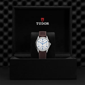 Front view of Tudor 1926 36mm steel watch with opaline dial, blue hands and brown leather strap in black Tudor box