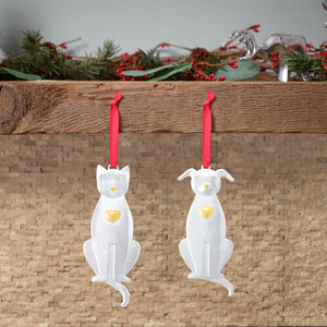 Two silver hanging pet ornaments — a cat and a dog — with gold heart details and red ribbons, suspended from a wooden shelf