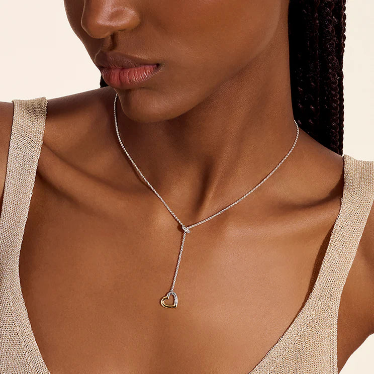 Close-up of Essential Heart Lariat Necklace with sterling silver chain and gold-accent heart pendant on neutral background