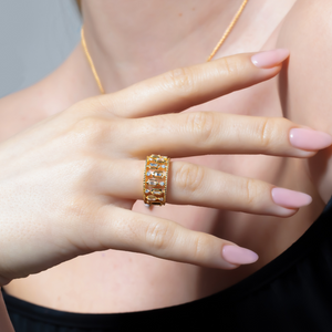 Close-up of a hand wearing a wide gold band ring set with rectangular baguette diamonds and milgrain detailing.