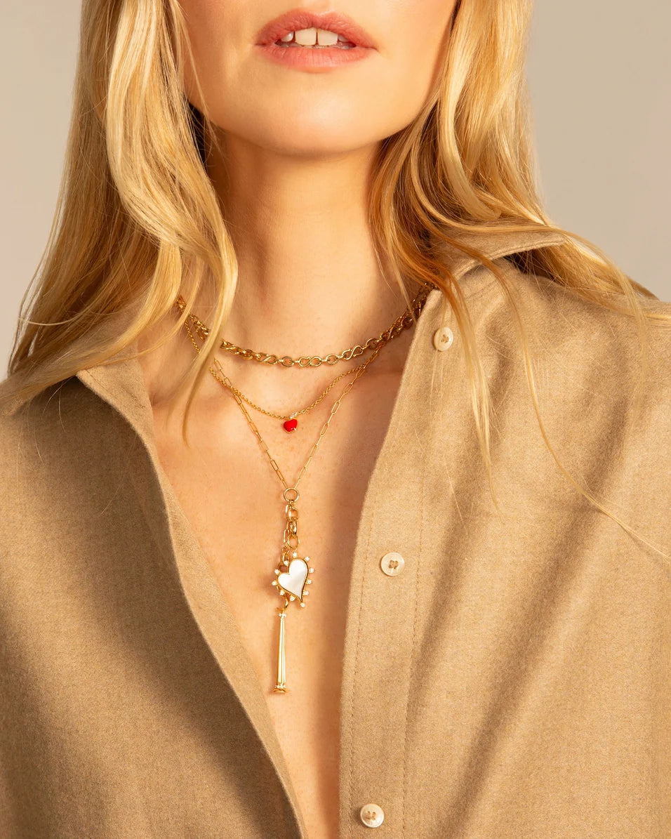 a woman wearing a tan shirt and multiple gold necklaces on a light grey background