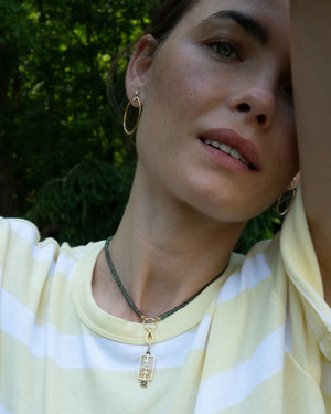 a woman wearing white and yellow striped tshirt with a green sapphire necklace with a gold charm