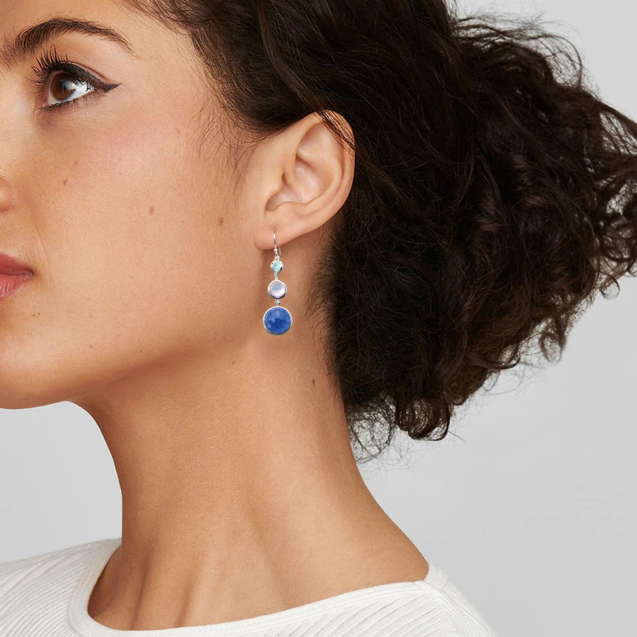 Side view of Lavanda 3-stone sterling silver drop earrings on model showing three graduated stones: light blue, pearl, deep blue on light gray background