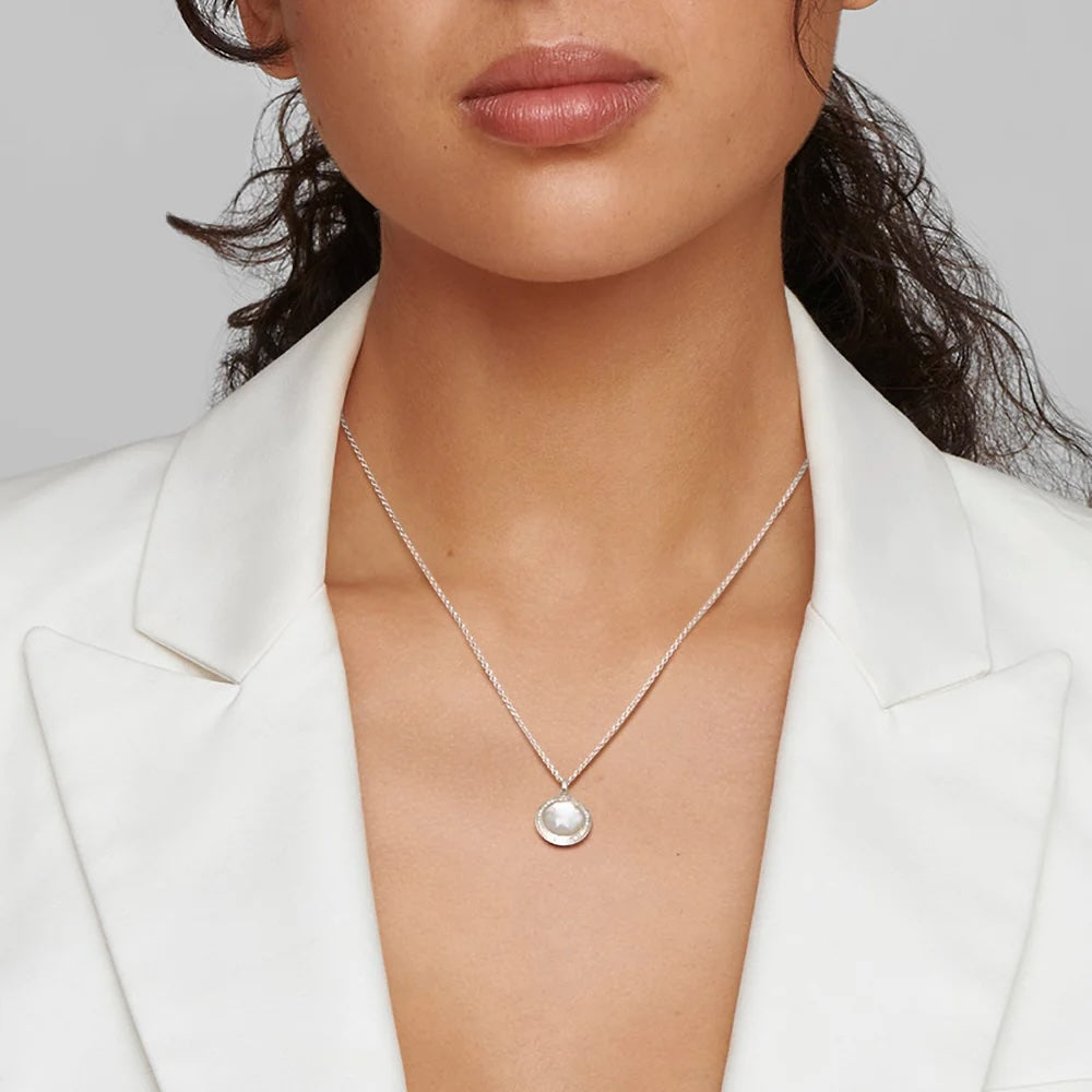 Front view of mini pendant necklace in sterling silver with mother-of-pearl center and diamond halo, worn at collarbone
