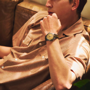 Man wearing a watch with a brown leather jacket sitting on a couch.