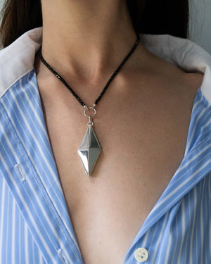 A woman with a blue striped shirt wearing a silver necklace with a black chain