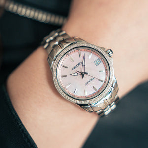 Wrist shot of Seiko SUR589 watch showcasing pink mother-of-pearl dial and diamond bezel on a stainless steel bracelet