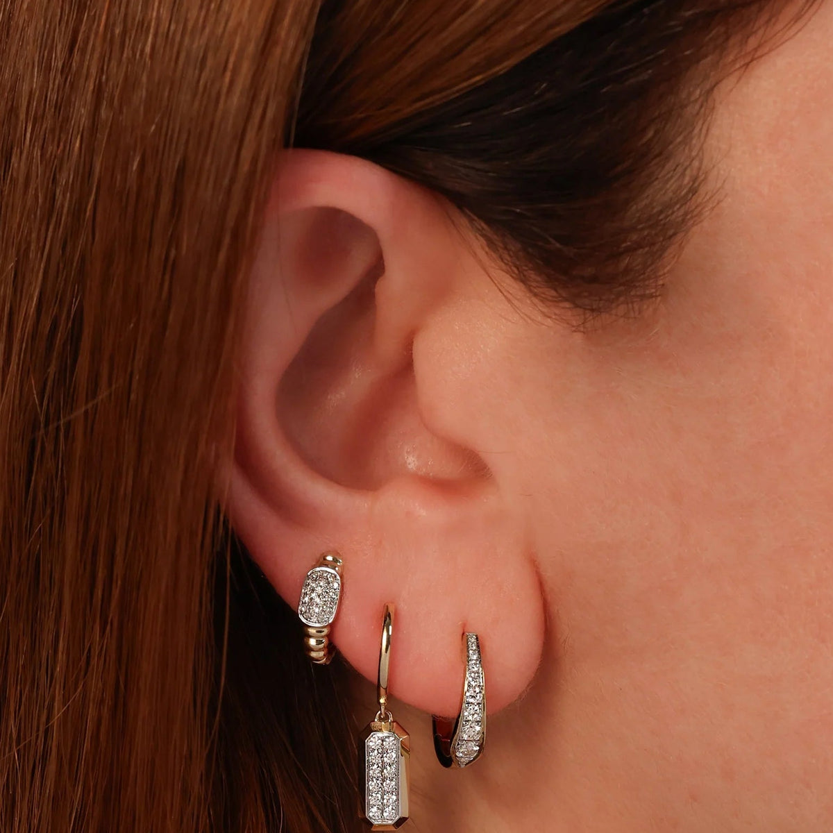 Close-up of left ear wearing 14K yellow gold huggie earring showcasing ribbed pave design and 0.11ctw diamonds on skin background