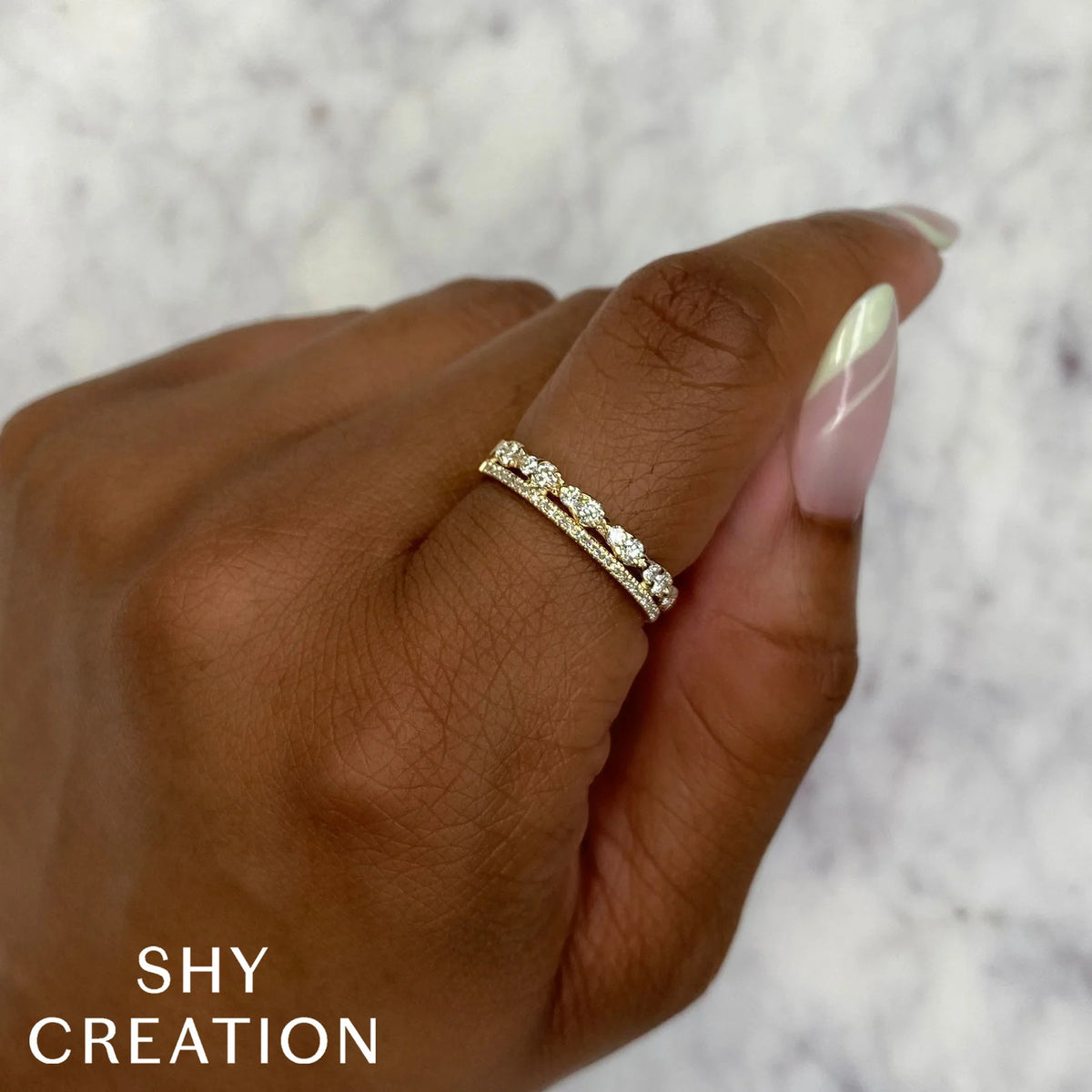 Close-up of two-row 14K yellow gold ring with 0.43 carat total weight of round diamonds worn on a model’s finger against a blurred marble background