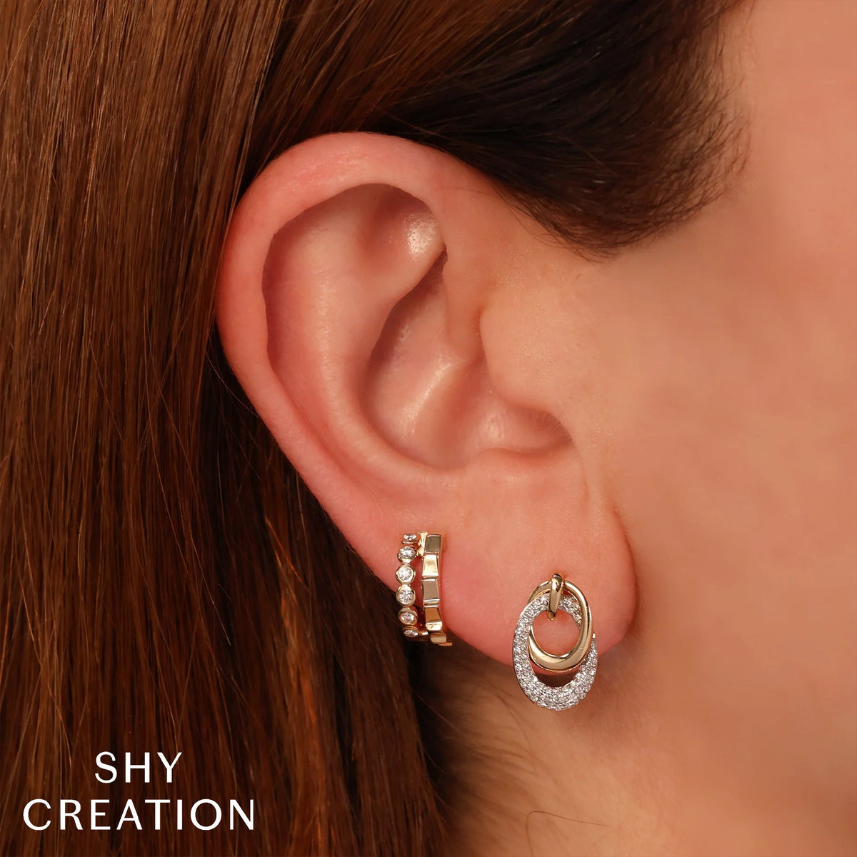 Close-up of 14K yellow gold oval earring showcasing pavé diamonds on a model’s ear with brown hair and Shy Creation logo visible