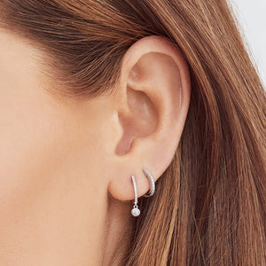 Right ear wearing two silver huggie hoop earrings: a pavé-set hoop and a smaller hoop with a bezel-set round diamond drop.