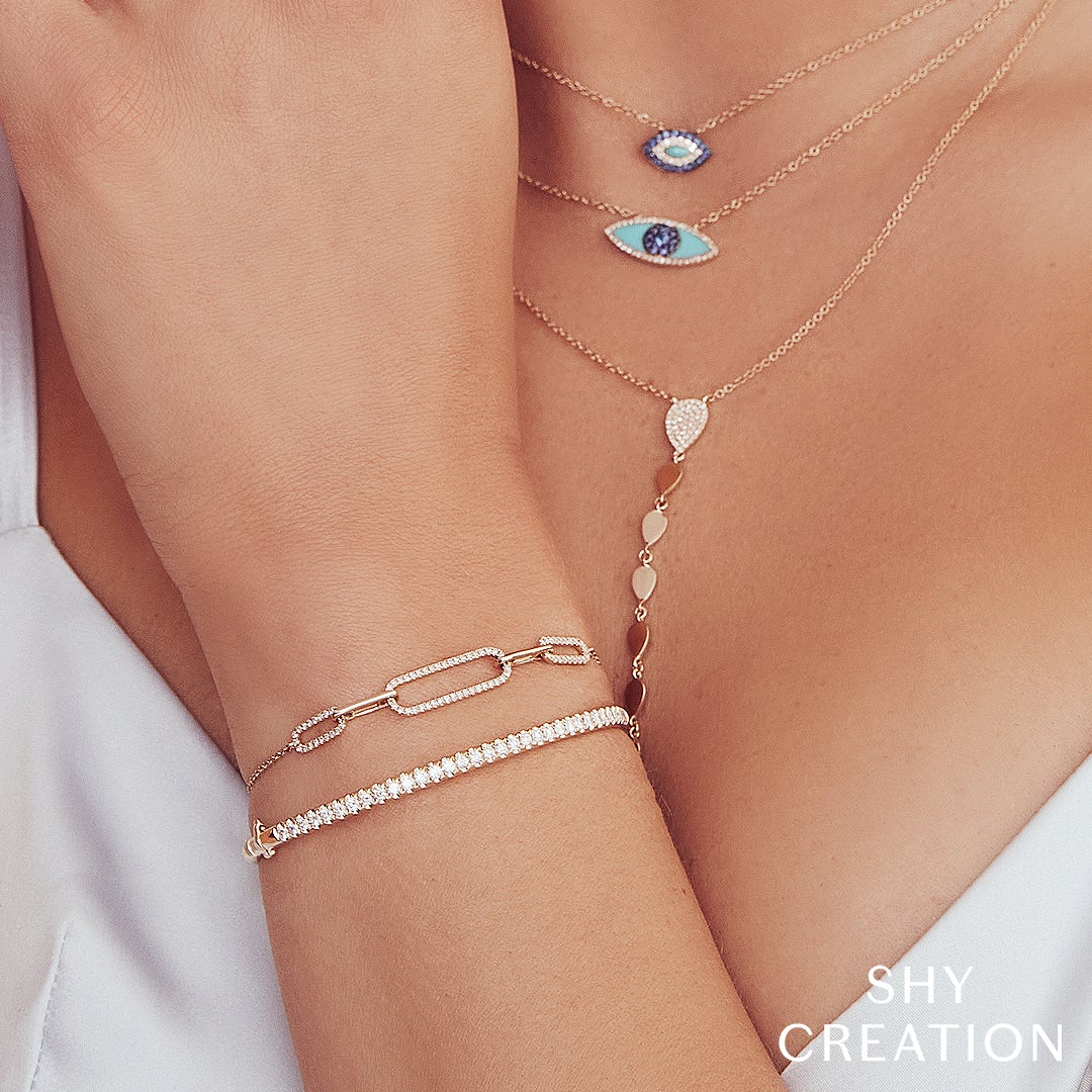 Close-up of 14K yellow gold 0.88ctw diamond bangle showing pave round diamonds on a model’s wrist with layered necklaces and white top