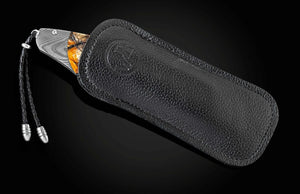 A folding pocket knife partially pulled from a black textured leather sheath with a braided cord lanyard, shown on a dark gradient background.