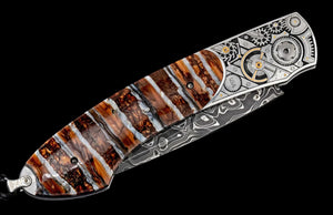 Close-up of William Henry B12 Watch Gears knife with mammoth-tooth handle, engraved gear bolsters and Damascus blade on black
