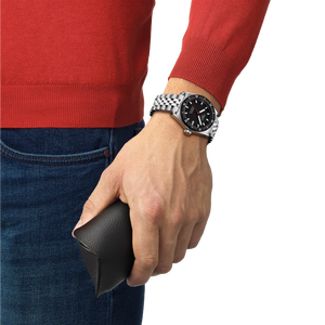 Hand wearing a silver watch holding a black wallet, with a red sweater and blue jeans.