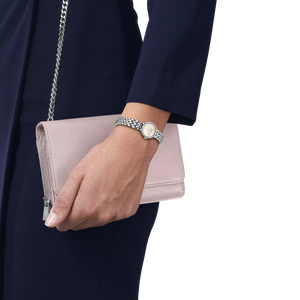 Hand holding a pink clutch bag with a silver chain, wearing a watch on a white background