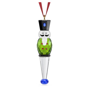green nutcracker ornament with red ribbon on a white background
