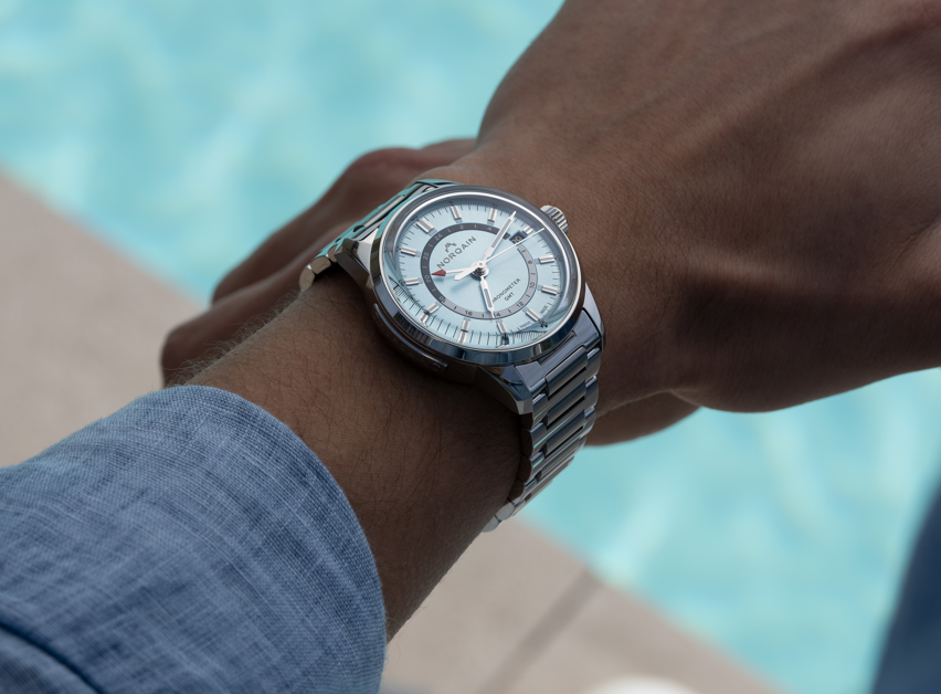 Angled view of Freedom 60 GMT 40mm watch on wrist showcasing stainless steel bracelet and light blue dial with poolside background