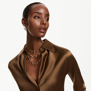 Woman wearing brown satin shirt and multicolored earrings and necklaces on a white background