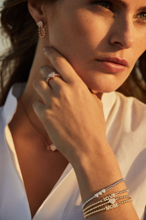 Close-up of model wrist wearing 18K yellow gold Tresore bracelets stacked with MOM and LOVE charms and a ring