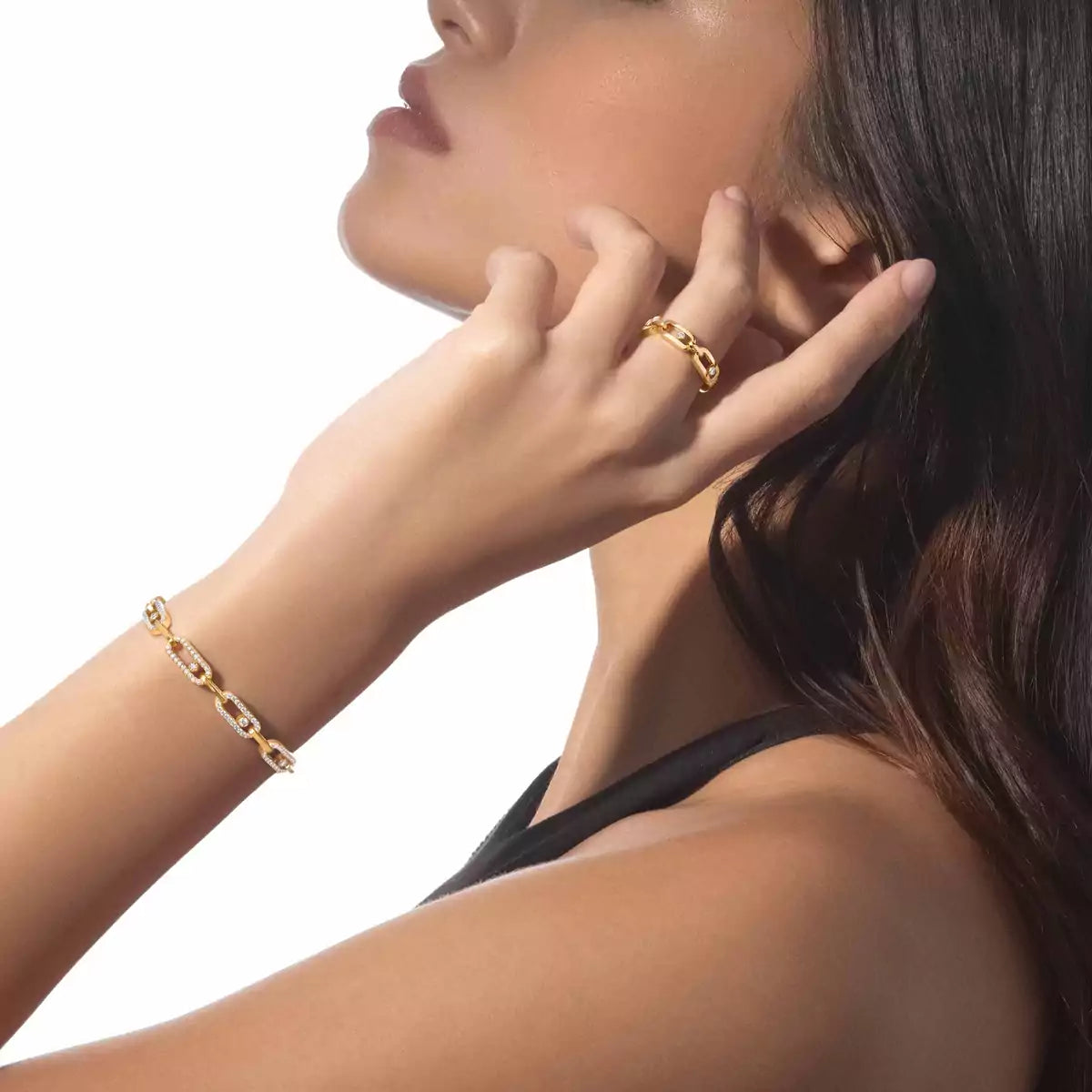 Woman wearing gold chain jewelry including an earring, ring, and bracelet on a white background