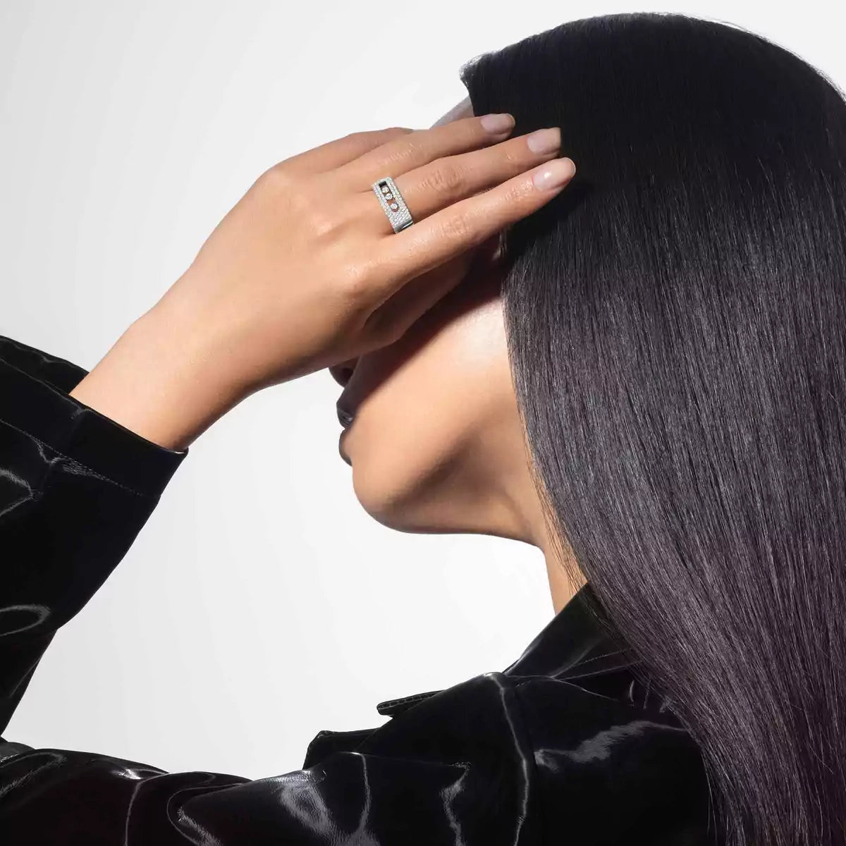Person wearing a ring with a diamond, touching their hair against a neutral background
