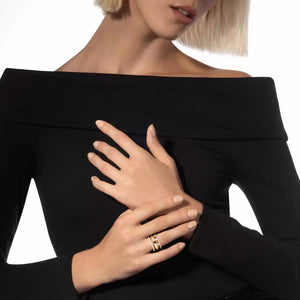 Woman wearing a black off-shoulder top with a gold ring on her finger against a white background