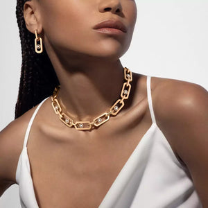 Woman wearing a gold chain necklace and earrings on a plain background